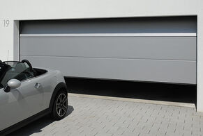 Leicht geöffnetes großes graues Garagen-Sektionaltor mit davor parkendem Mini-Cabrio