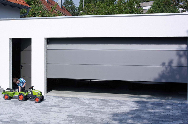 Kind mit kettcar vor einem grauen Garagentor mit Nebentür